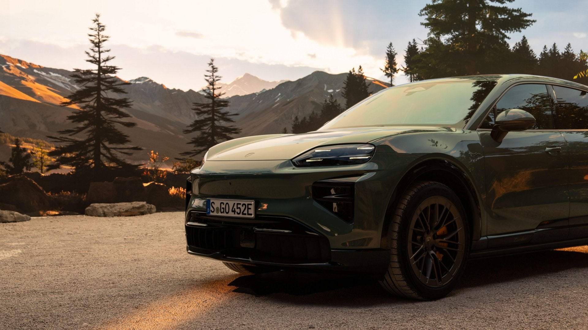 2026 Porsche Cayenne Turbo Electric in green parked in a mountain setting at dusk, highlighting its modern headlights and aggressive front design.