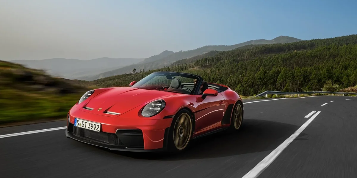 Red Porsche 911 GT3 RS Cabriolet driving on mountain road from front angle.